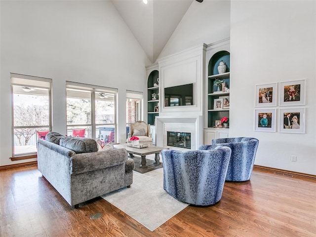 living room featuring high vaulted ceiling, wood finished floors, a wealth of natural light, and a glass covered fireplace