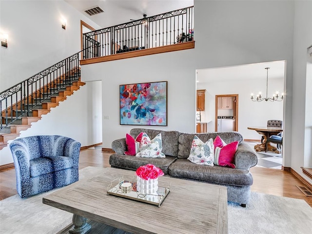 living room with visible vents, a towering ceiling, wood finished floors, a chandelier, and baseboards