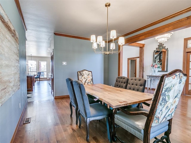 dining space with a chandelier, wood finished floors, visible vents, baseboards, and ornamental molding