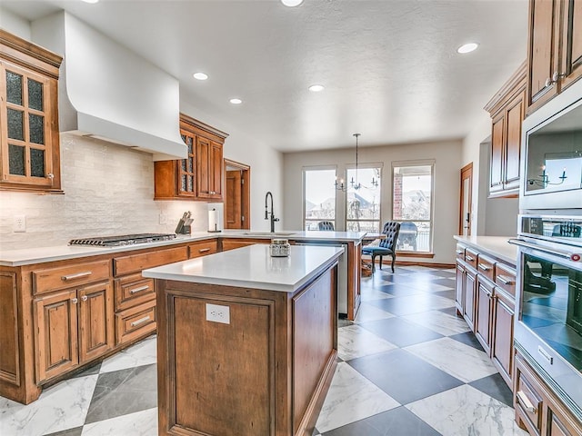 kitchen featuring custom range hood, appliances with stainless steel finishes, brown cabinets, a peninsula, and a sink