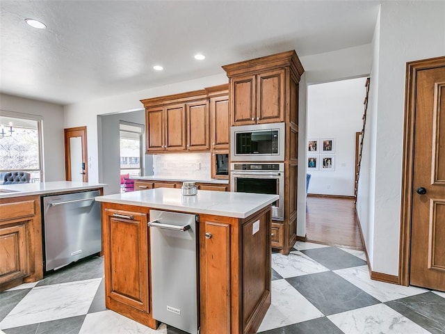 kitchen featuring stainless steel appliances, light countertops, backsplash, a center island, and brown cabinetry