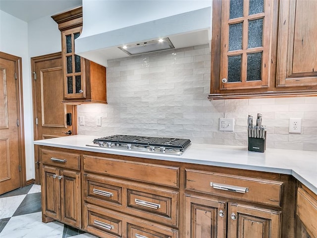 kitchen with stainless steel gas cooktop, custom exhaust hood, brown cabinets, and light countertops