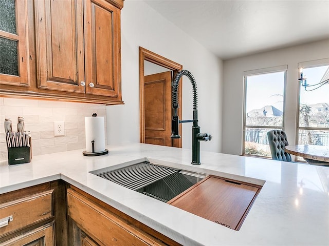 kitchen featuring brown cabinetry, glass insert cabinets, a sink, and decorative backsplash