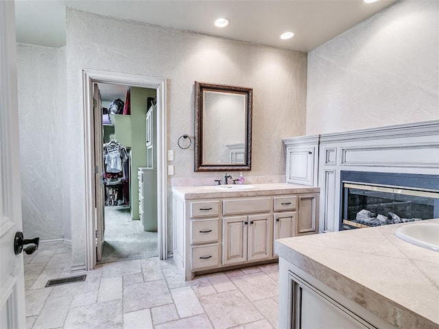 full bath with stone tile floors, recessed lighting, visible vents, a glass covered fireplace, and vanity