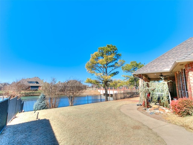 view of yard with a water view, ceiling fan, and a fenced backyard