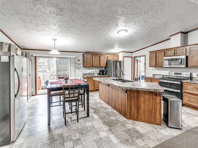 kitchen featuring a center island with sink, brown cabinetry, stainless steel appliances, crown molding, and a sink