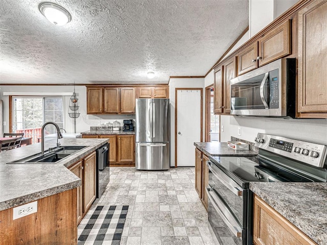 kitchen with appliances with stainless steel finishes, brown cabinets, stone finish flooring, a kitchen island with sink, and a sink