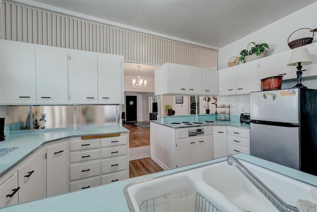 kitchen with freestanding refrigerator, a chandelier, white cabinetry, wood finished floors, and light countertops