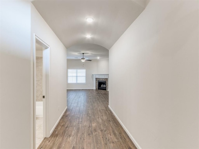 corridor with arched walkways, baseboards, vaulted ceiling, and wood finished floors