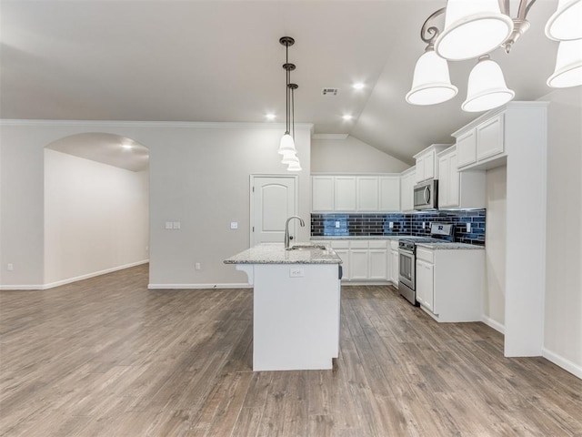 kitchen with arched walkways, a sink, appliances with stainless steel finishes, light wood-type flooring, and backsplash