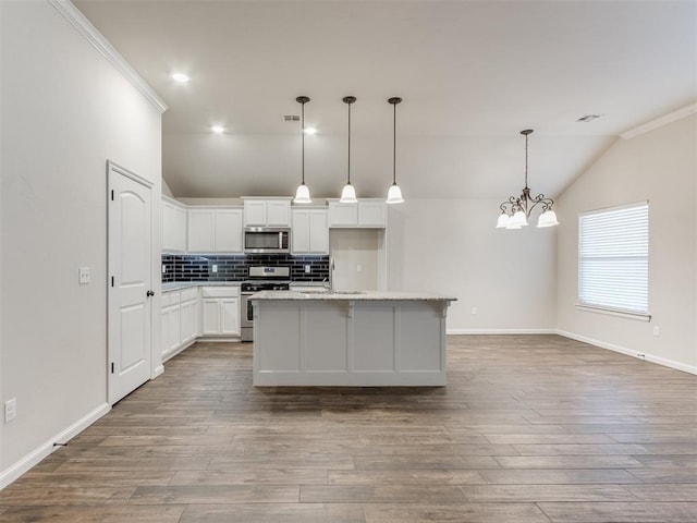 kitchen with lofted ceiling, stainless steel appliances, wood finished floors, white cabinets, and backsplash