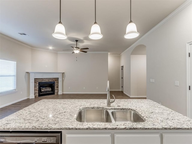 kitchen with arched walkways, a fireplace, white cabinets, a sink, and dishwasher