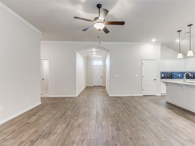 unfurnished living room with a ceiling fan, arched walkways, ornamental molding, and light wood-style flooring