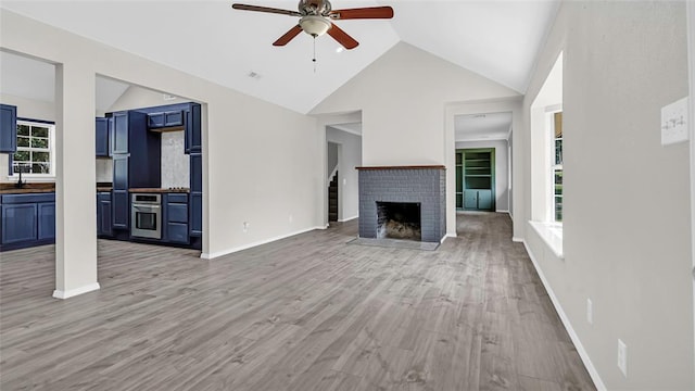 unfurnished living room featuring a brick fireplace, baseboards, a ceiling fan, light wood-style floors, and a sink