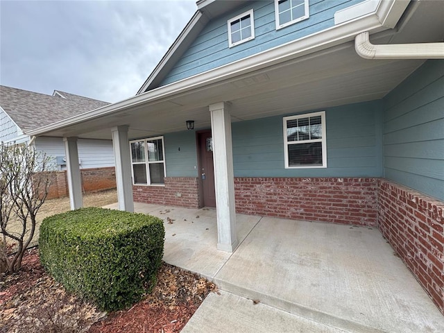 property entrance featuring brick siding, a porch, and roof with shingles