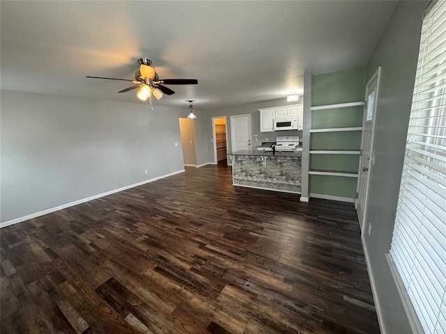 unfurnished living room featuring dark wood finished floors, baseboards, and ceiling fan