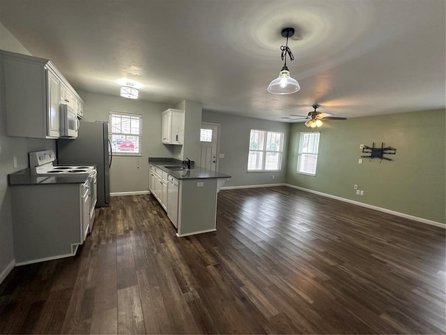 kitchen featuring dark countertops, open floor plan, a peninsula, white appliances, and a sink