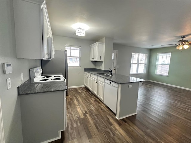 kitchen featuring white appliances, baseboards, a peninsula, dark wood-style flooring, and a sink