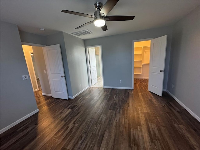 unfurnished bedroom with a spacious closet, visible vents, baseboards, and dark wood-style flooring