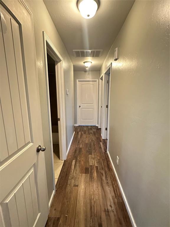 hallway featuring dark wood-style floors, visible vents, and baseboards