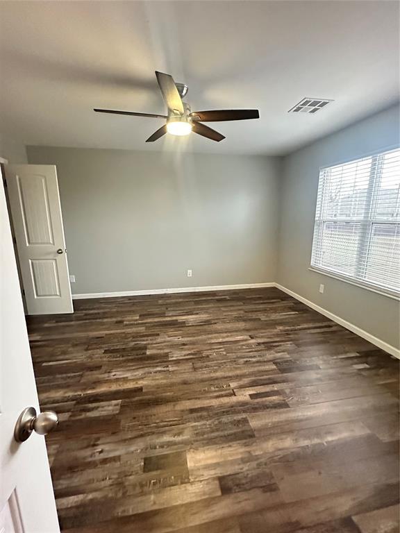 unfurnished room featuring dark wood finished floors, visible vents, ceiling fan, and baseboards