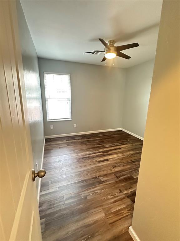 empty room with dark wood finished floors, ceiling fan, and baseboards