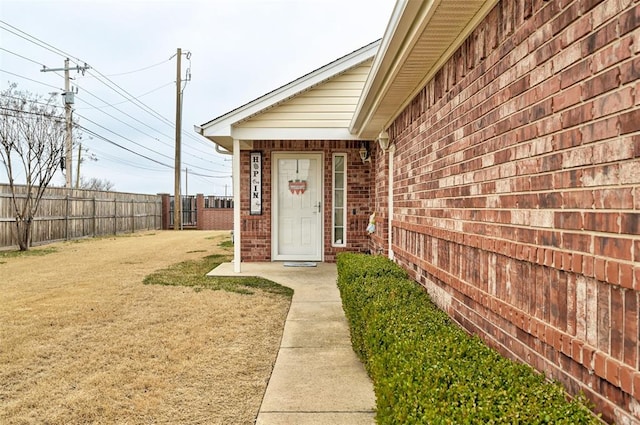 view of exterior entry featuring brick siding, fence, and a lawn