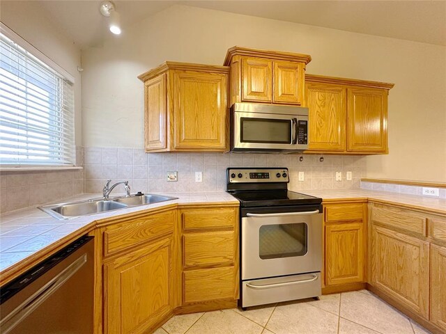 kitchen featuring tile countertops, stainless steel appliances, a sink, and light tile patterned flooring