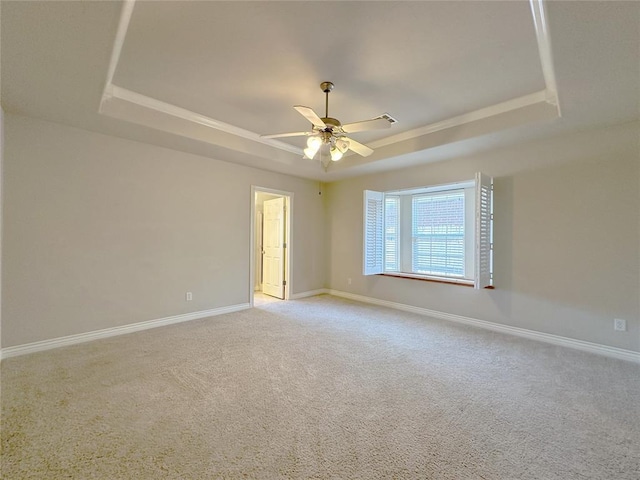 carpeted spare room featuring a tray ceiling, a ceiling fan, and baseboards