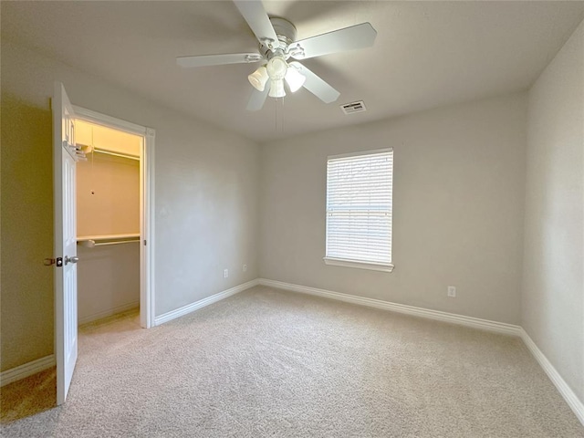 unfurnished bedroom featuring light carpet, visible vents, baseboards, and a walk in closet