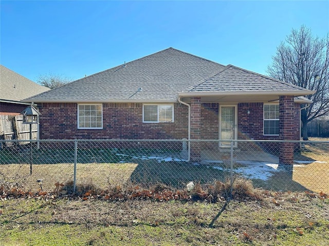 back of property with a shingled roof, fence, and brick siding