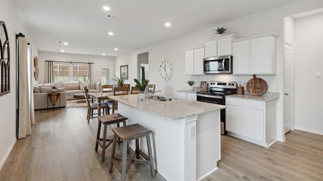 kitchen with visible vents, appliances with stainless steel finishes, a kitchen island with sink, white cabinetry, and a sink