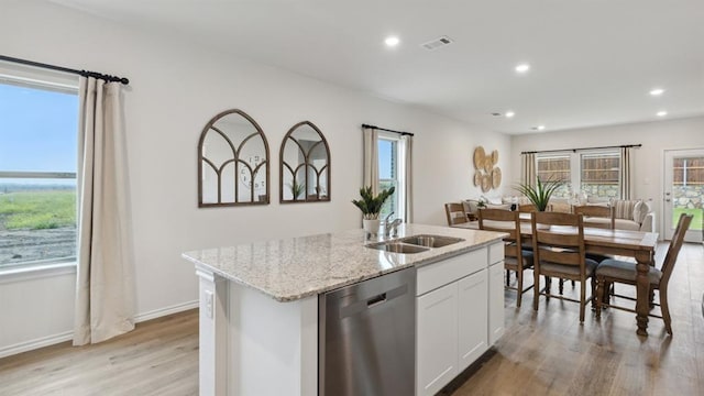 kitchen featuring visible vents, dishwasher, light stone counters, light wood-style floors, and a sink