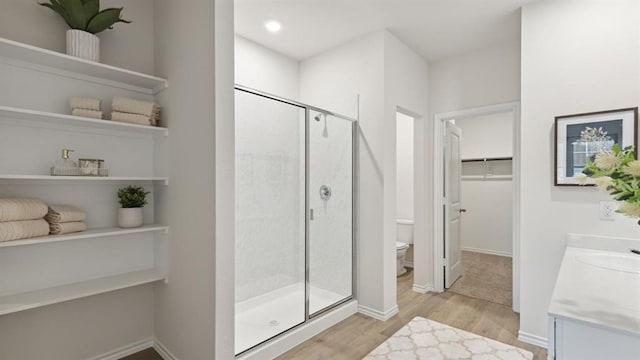 full bathroom with a stall shower, toilet, wood finished floors, a spacious closet, and vanity