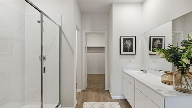 bathroom featuring a walk in closet, a shower stall, vanity, and wood finished floors