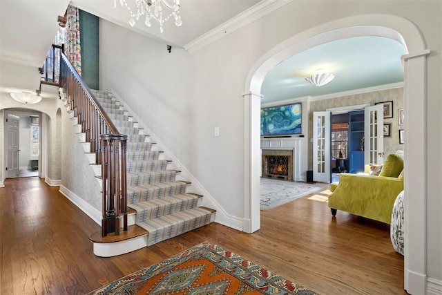 foyer with arched walkways, wood finished floors, baseboards, a lit fireplace, and crown molding