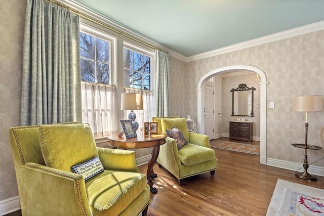 sitting room with arched walkways, ornamental molding, wood finished floors, baseboards, and wallpapered walls