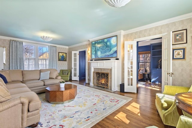 living room featuring french doors, a fireplace, crown molding, wood finished floors, and wallpapered walls