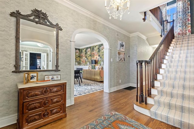 foyer with baseboards, arched walkways, stairway, ornamental molding, and wood finished floors