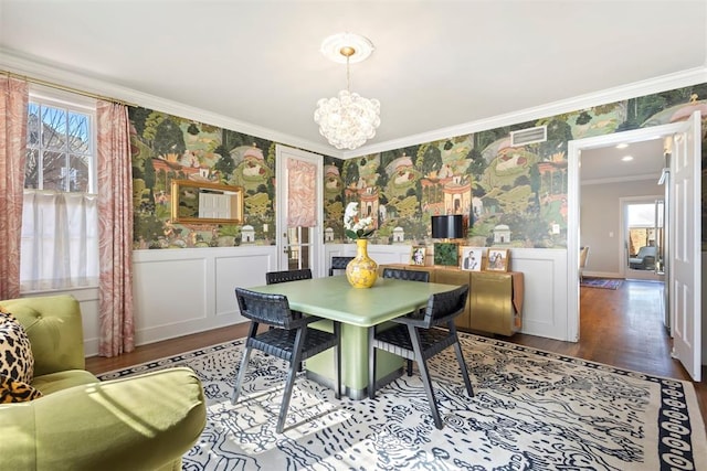 dining room featuring wallpapered walls, wainscoting, ornamental molding, wood finished floors, and an inviting chandelier