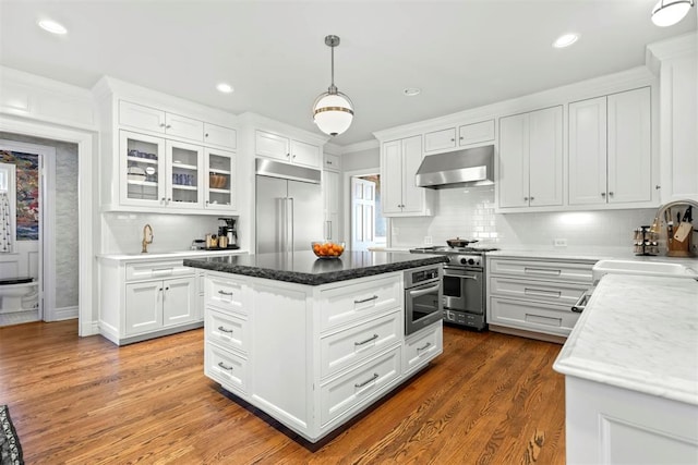 kitchen featuring premium appliances, under cabinet range hood, a sink, white cabinets, and dark wood-style floors