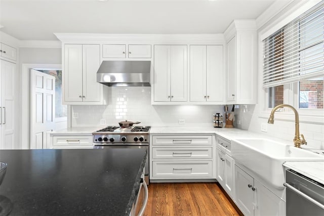 kitchen with dark wood-style floors, wall chimney exhaust hood, stainless steel appliances, white cabinetry, and a sink