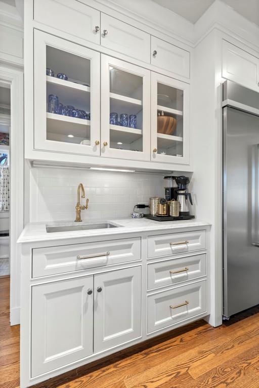 bar featuring built in fridge, a sink, light wood-style flooring, and decorative backsplash