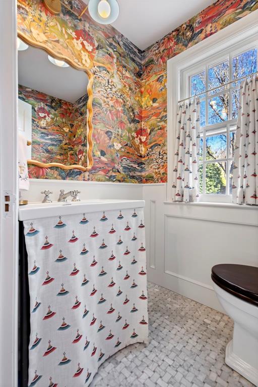 bathroom with toilet, wallpapered walls, and a wainscoted wall