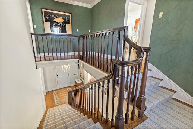 stairway featuring baseboards, ornamental molding, wood finished floors, and wallpapered walls