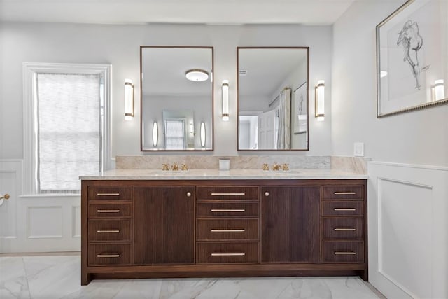 full bath with double vanity, a wainscoted wall, marble finish floor, a decorative wall, and a sink