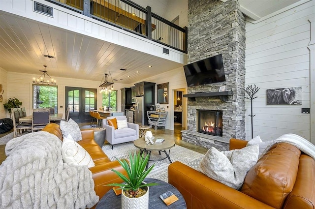 living area featuring a fireplace, a towering ceiling, wood ceiling, wood walls, and a chandelier