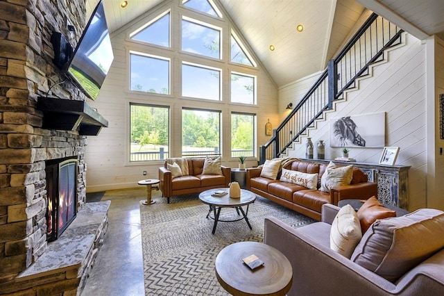 living area featuring stairway, finished concrete floors, wood walls, a fireplace, and high vaulted ceiling