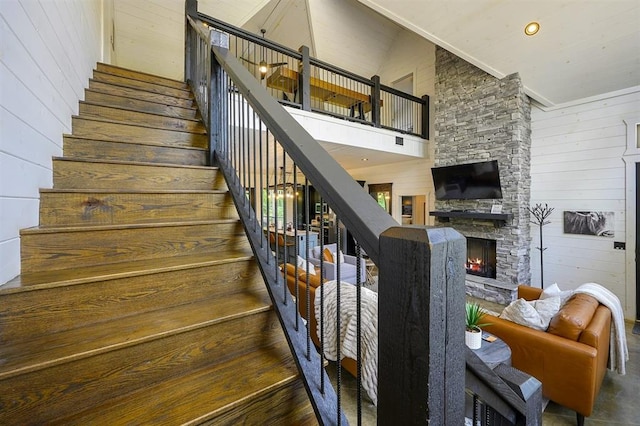 stairs featuring recessed lighting, wood walls, a stone fireplace, and a high ceiling