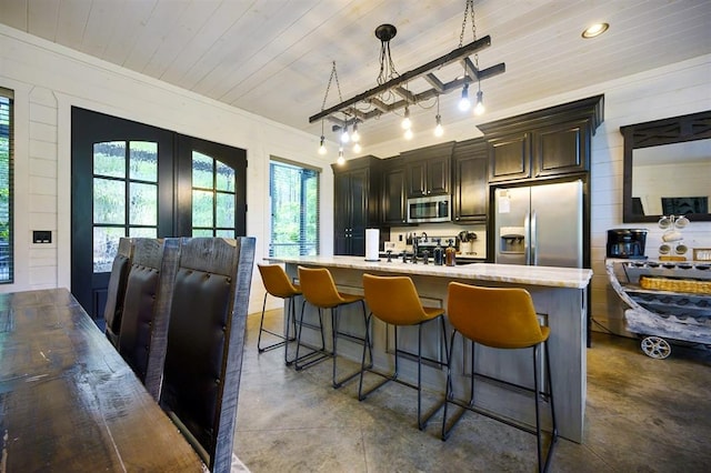 kitchen featuring a center island with sink, finished concrete flooring, stainless steel appliances, wood ceiling, and a kitchen breakfast bar